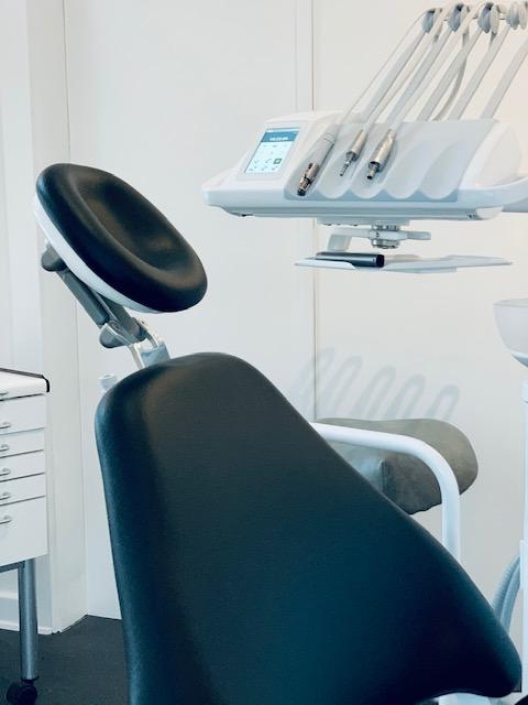 Et moderne tandlægestol med en ergonomisk ryg og tandlægeudstyr i baggrunden.