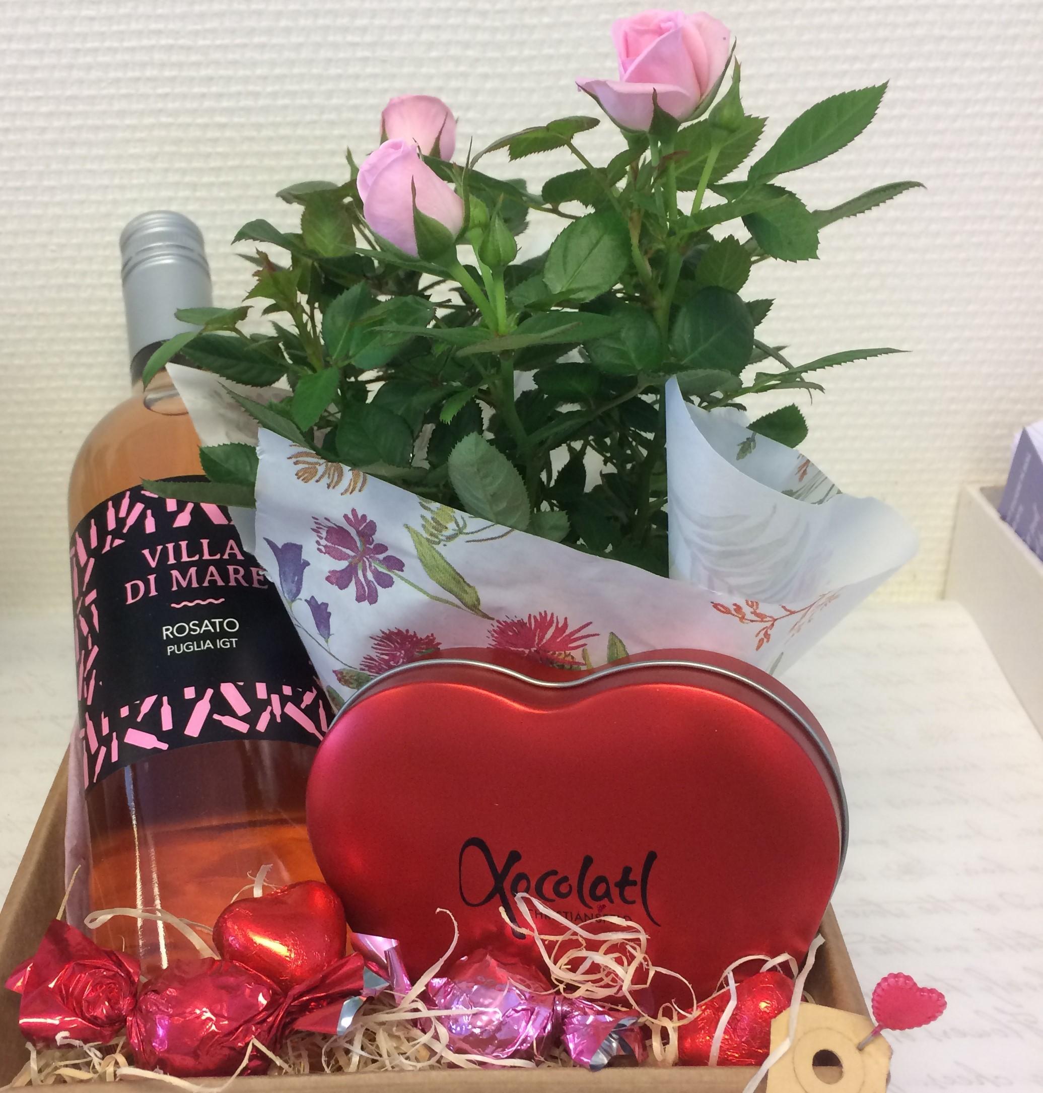 En gavekurv med rosévin, en buket lyserøde roser, chokolade i hjerteform og dekorationer.