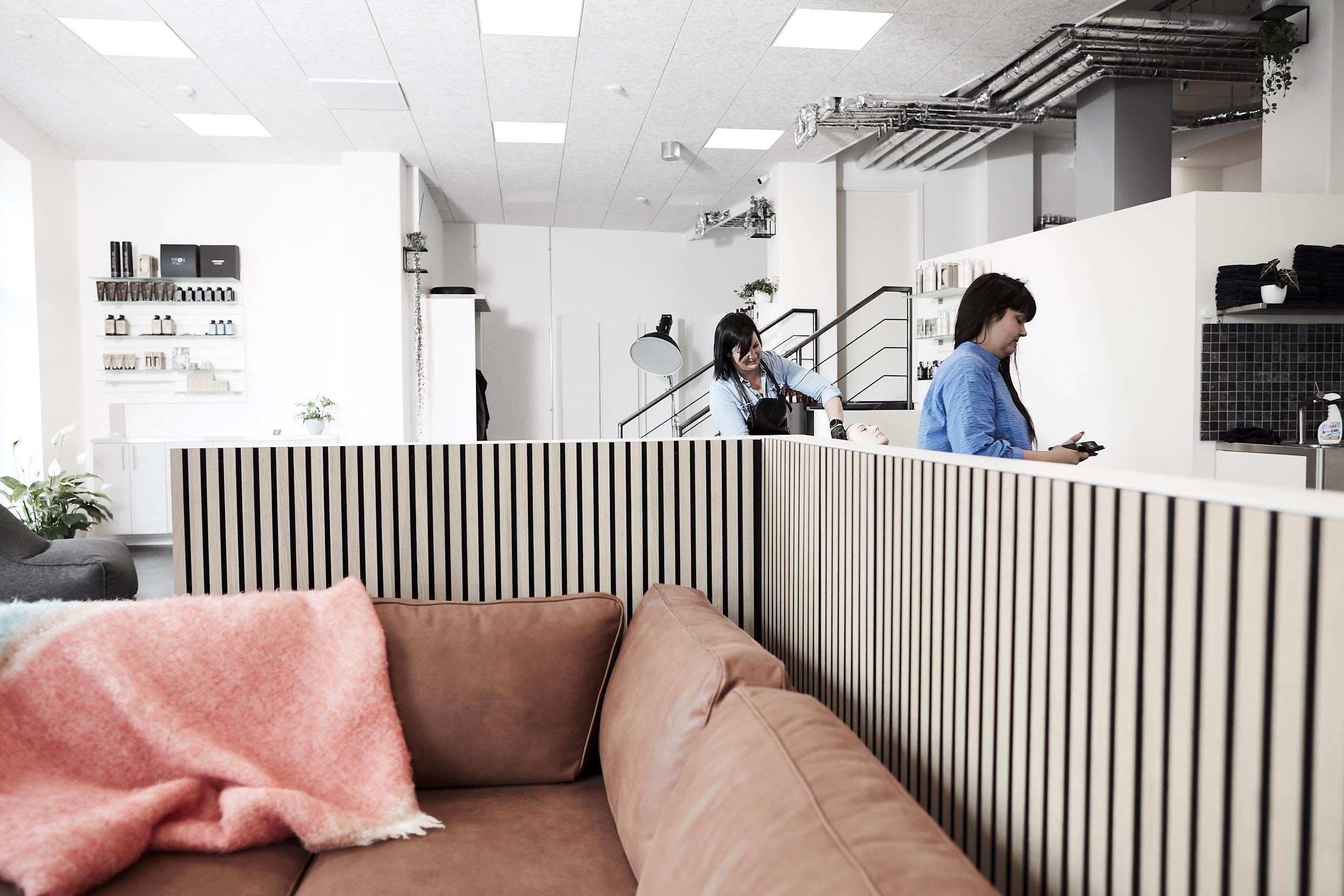 Moderne kontormiljø med en sofa, en kvinde der arbejder, og en anden person i baggrunden.