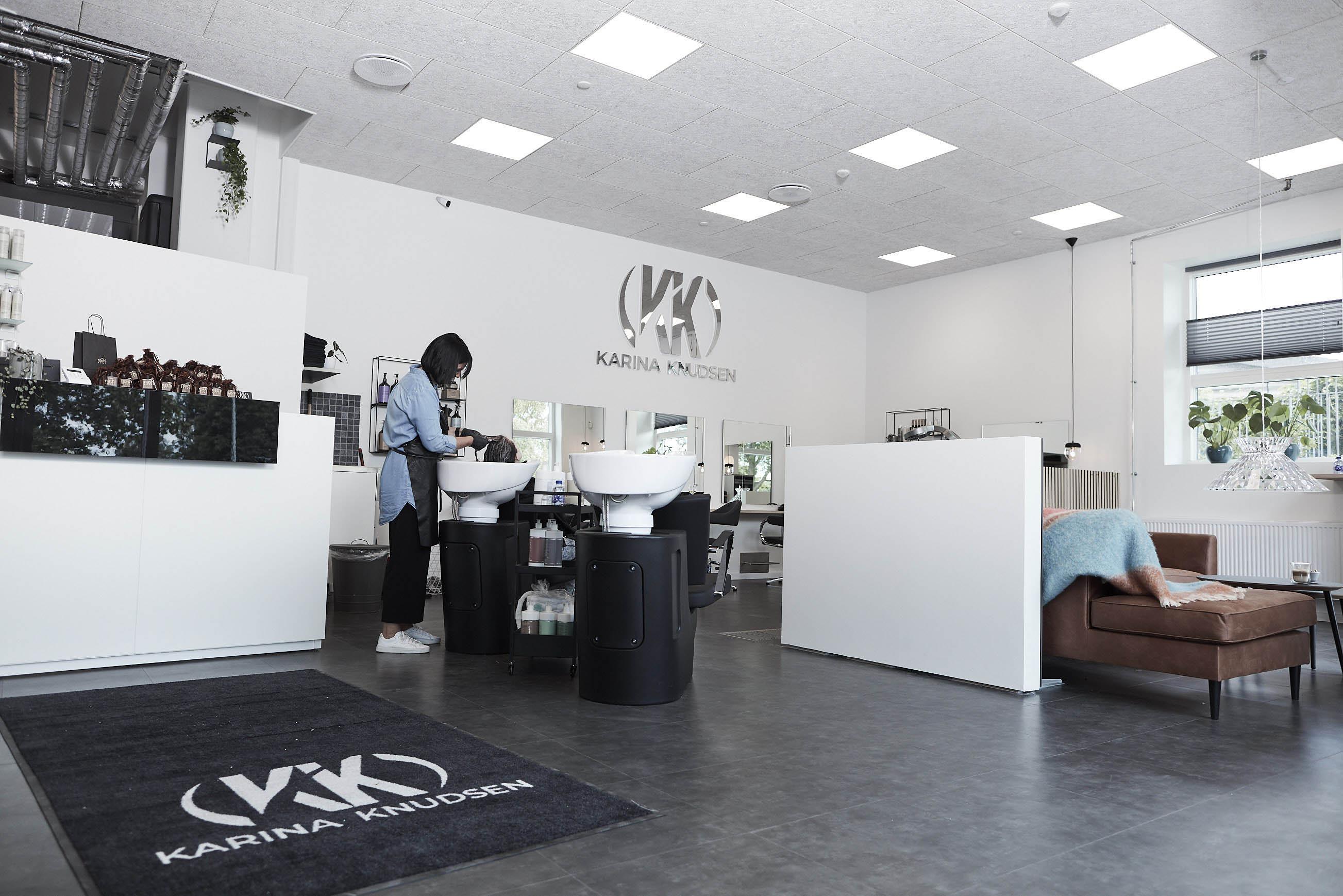En frisørsalon med moderne indretning, hvor en frisør arbejder ved en vaskestation.