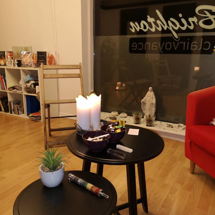 Et hyggeligt rum med stearinlys, små borde, en plante og en statue, der skaber en afslappende atmosfære.