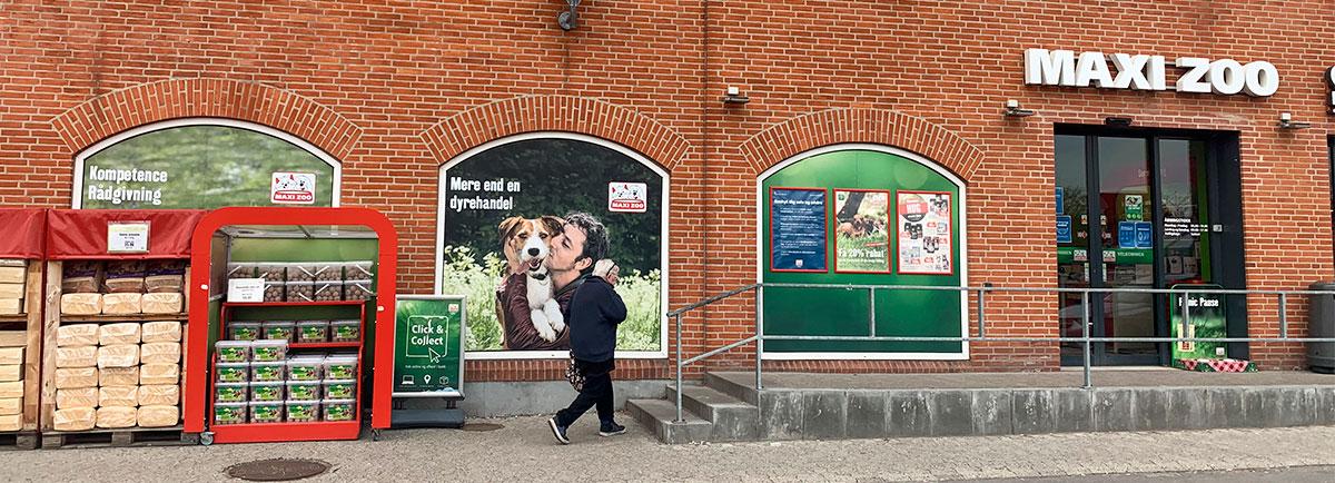 En person går forbi MAXI ZOO med dyrefoder og reklamer på væggene.
