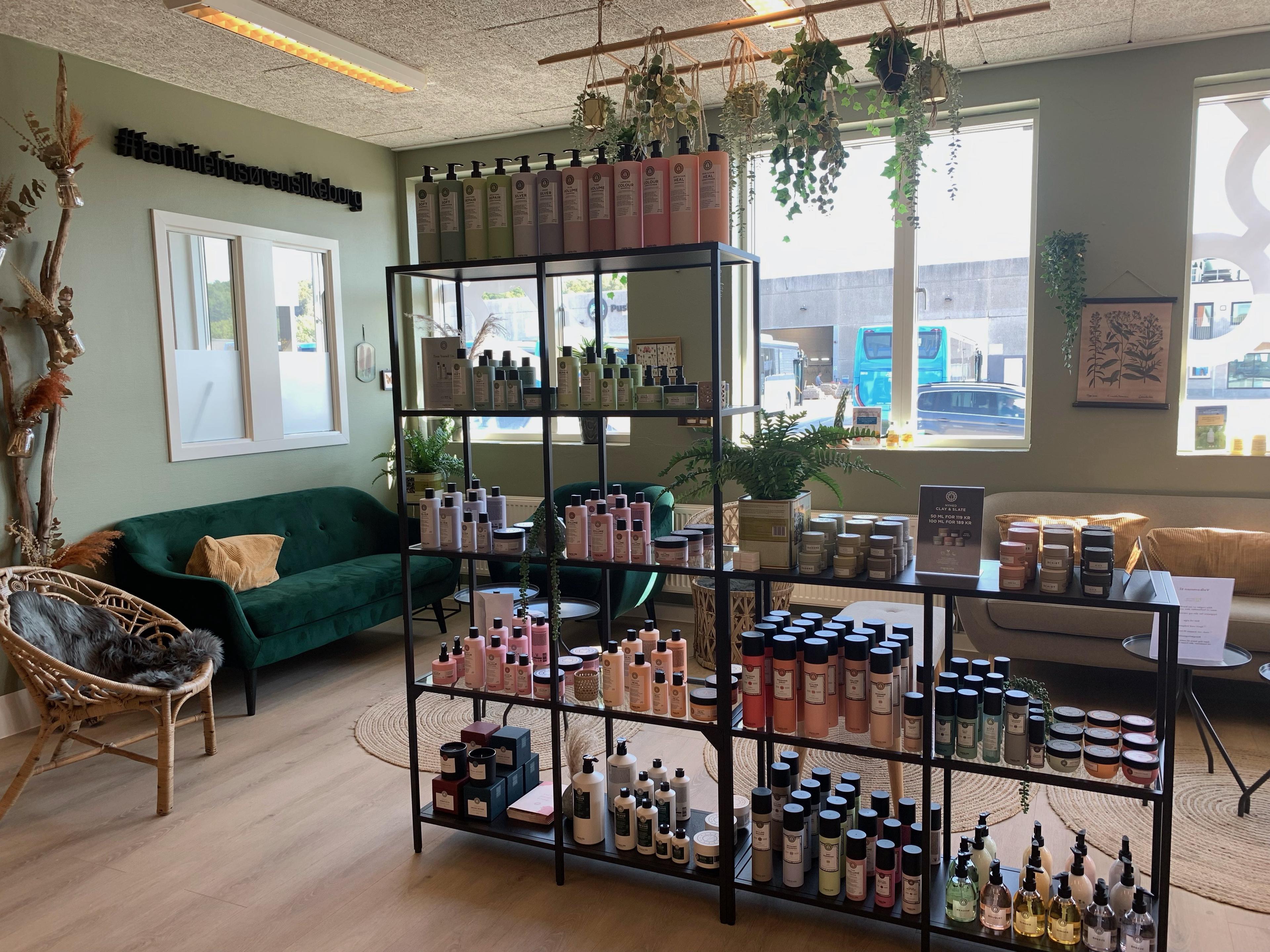 Indendørs butik med hylder fyldt med skønhedsprodukter, planter og en grøn sofa i et lyst rum.