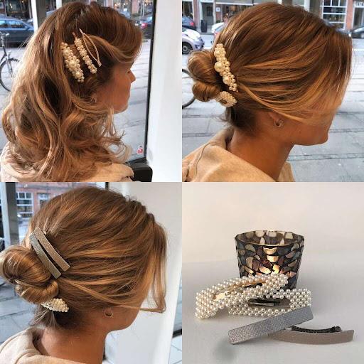 En kvinde med bølget hår og perleaccessories i håret, der sidder ved et vindue med lys.