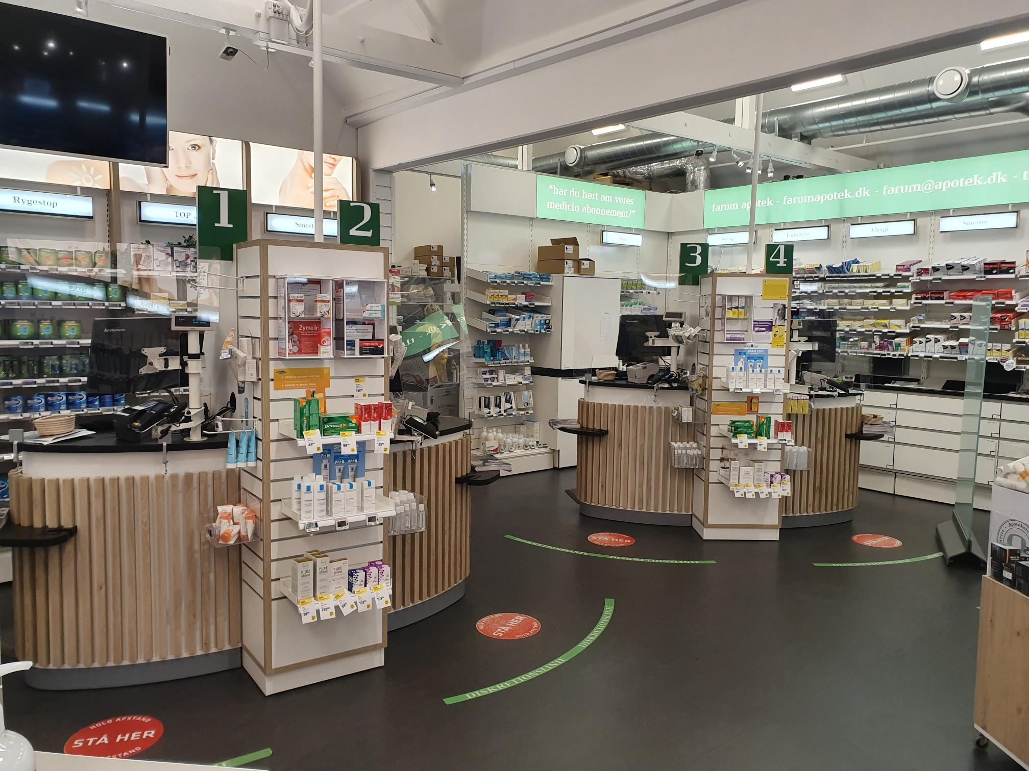 Apotek med flere diske, hylder med medicin og sundhedsprodukter samt skiltning til kunder.
