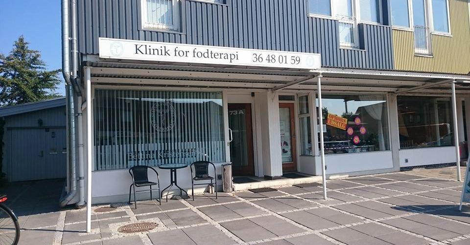 Klinik for fodterapi med skilt og udendørs borde og stole foran bygningen.