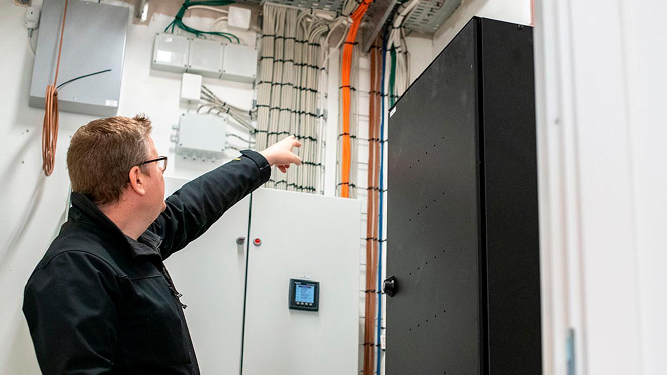 En tekniker peger på elektriske installationer i et teknisk rum med skabs- og ledningssystemer.