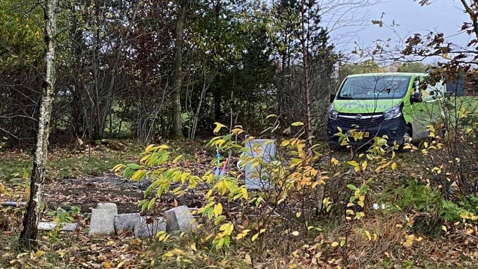 En grøn varevogn parkeret i en skov med efterårsblade og en lille byggeplads i forgrunden.