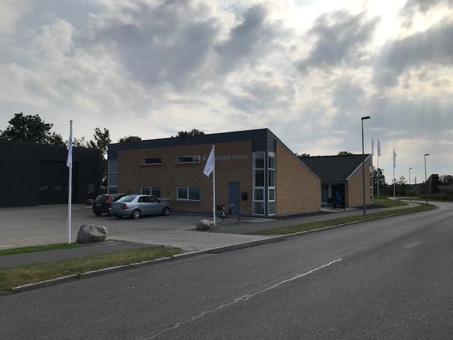 En moderne bygning med mursten og store vinduer, beliggende ved en vej med biler og flag.