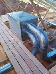 Ventilationsanlæg med metalrør installeret på et tag, omgivet af træbjælker.