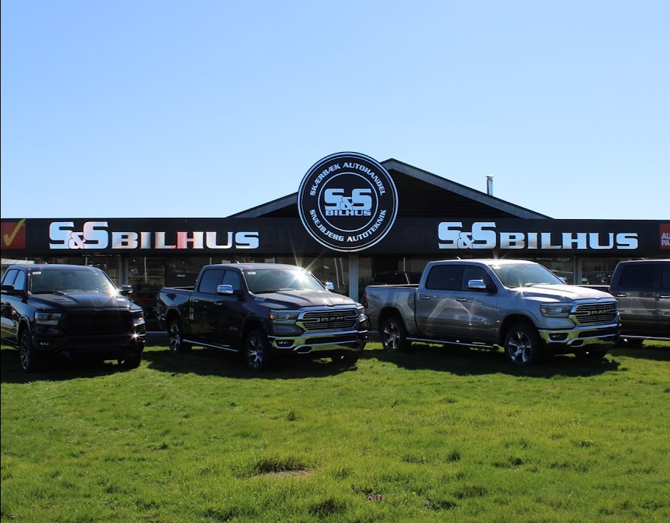 Tre pickupbiler parkeret foran S&S Bilhus med en klar blå himmel i baggrunden.