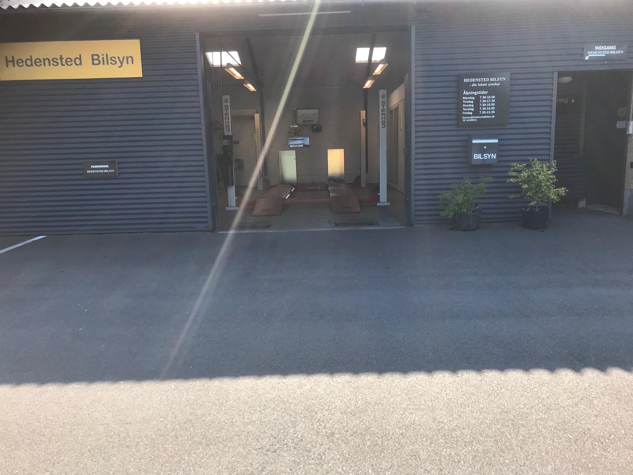 Facade af Hejlsminde Bilsyn med åbne døre og planter foran.