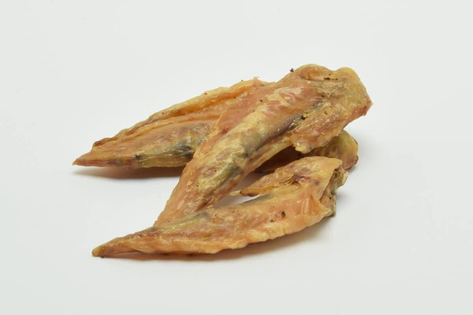 Tørrede fiskesnacks i form af spidse stykker, der ligger på en hvid baggrund.