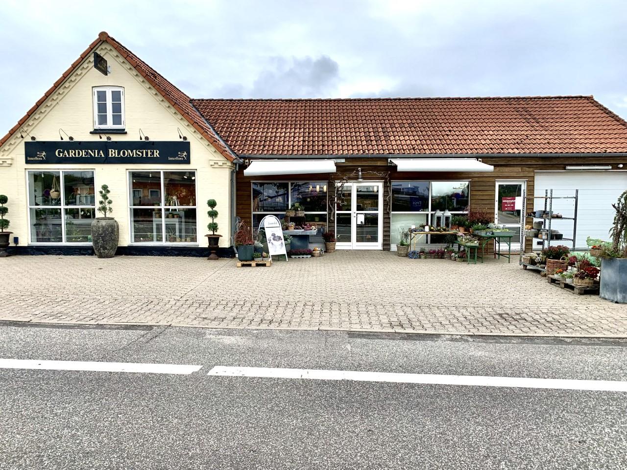 En blomsterbutik med en rød tag og store vinduer, omgivet af planter og dekorationer.