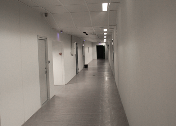 En lang, hvid gang med døre på begge sider og blødt lys i loftet.