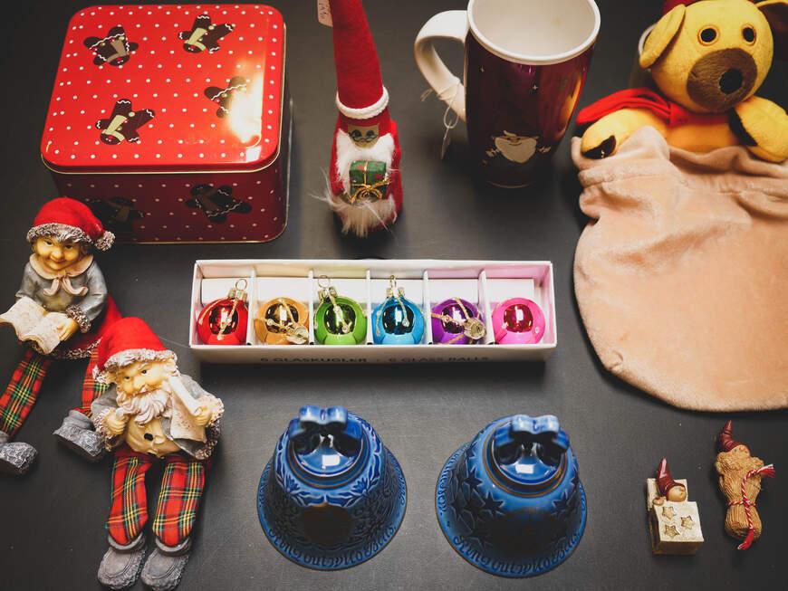 En samling af julepynt, herunder nisser, klokker, en kop, en bamse og en rød kagedåse.