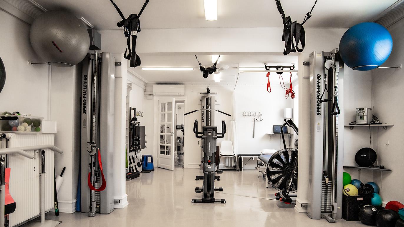 Træningslokale med fitnessudstyr, herunder vægte, træningsmaskiner og bolde til styrketræning.