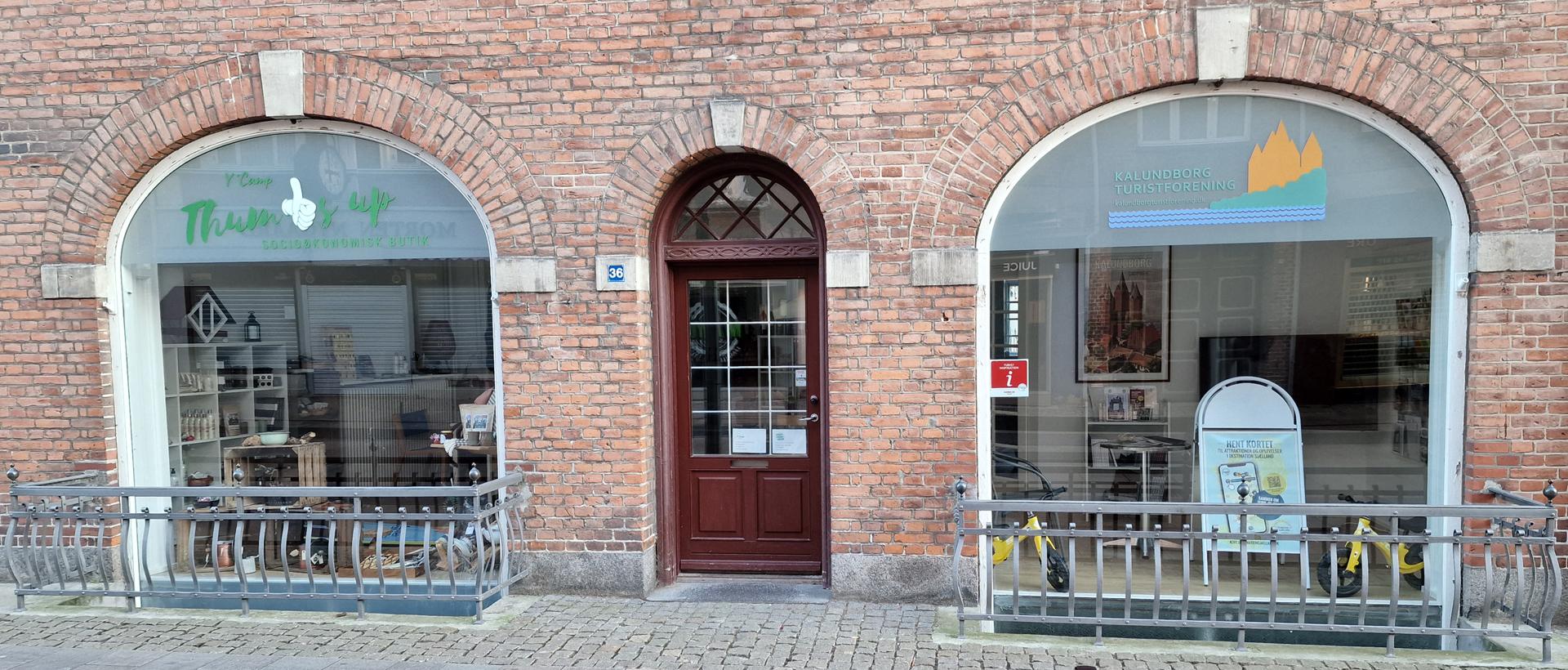Butiksvinduer med træfacade og kunstudstillinger i en murstensbygning.