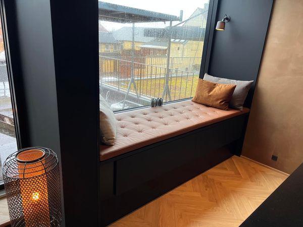 En hyggelig vindueskarm med puder, en lampe og en kurv, der giver en varm atmosfære i rummet.