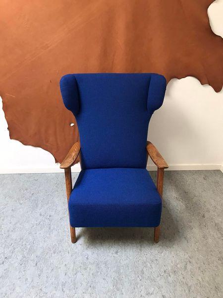 Blå lænestol med træarme placeret foran en brun vægdekoration.