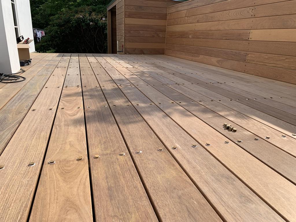 Nybehandlet træterrasse med sollys og skygger, der fremhæver de glatte planker og naturlige farver.