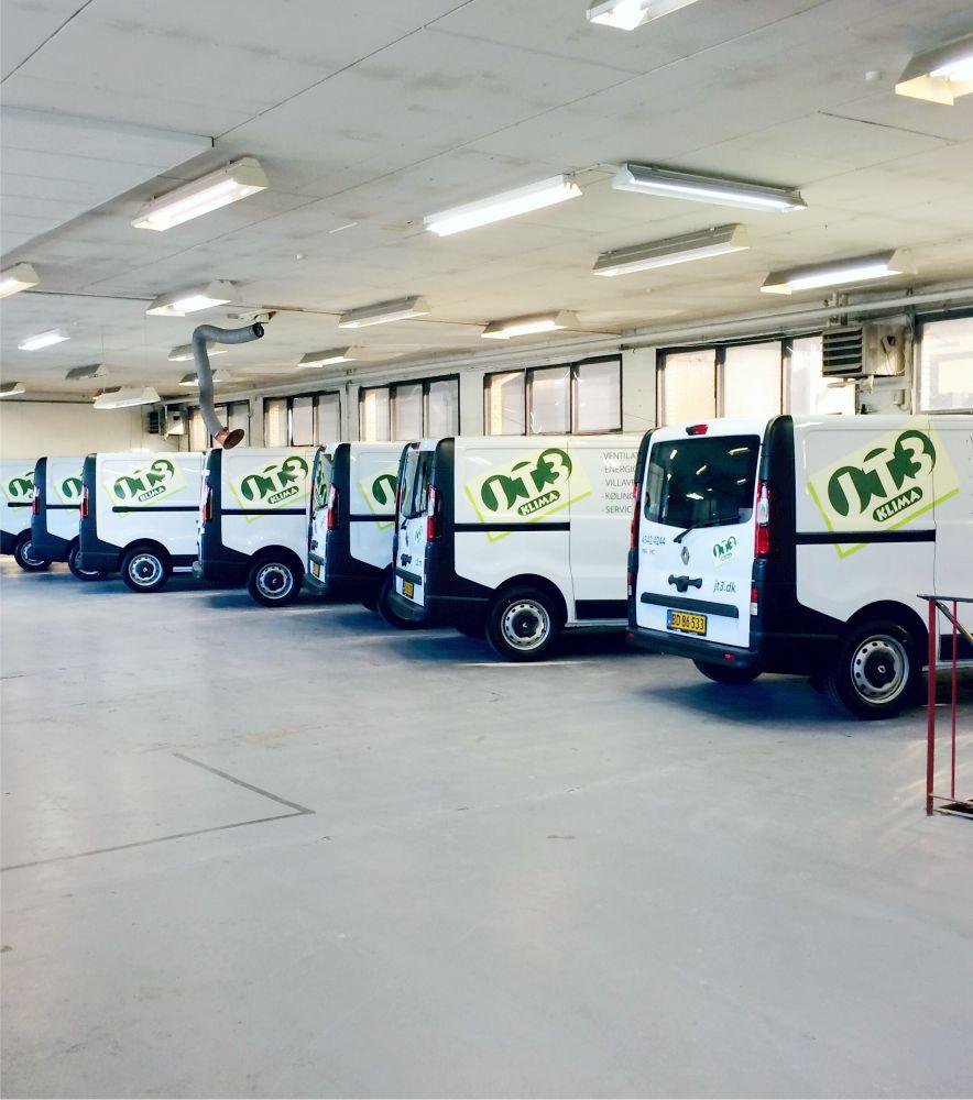 Flere varevogne parkeret i en garage med logoer på bagsiden, klar til levering.