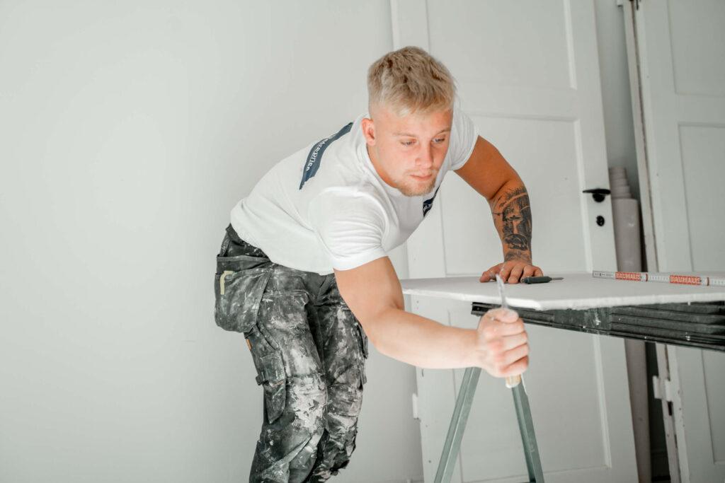 En maler arbejder koncentreret ved et bord i et lyst rum med hvid væg.
