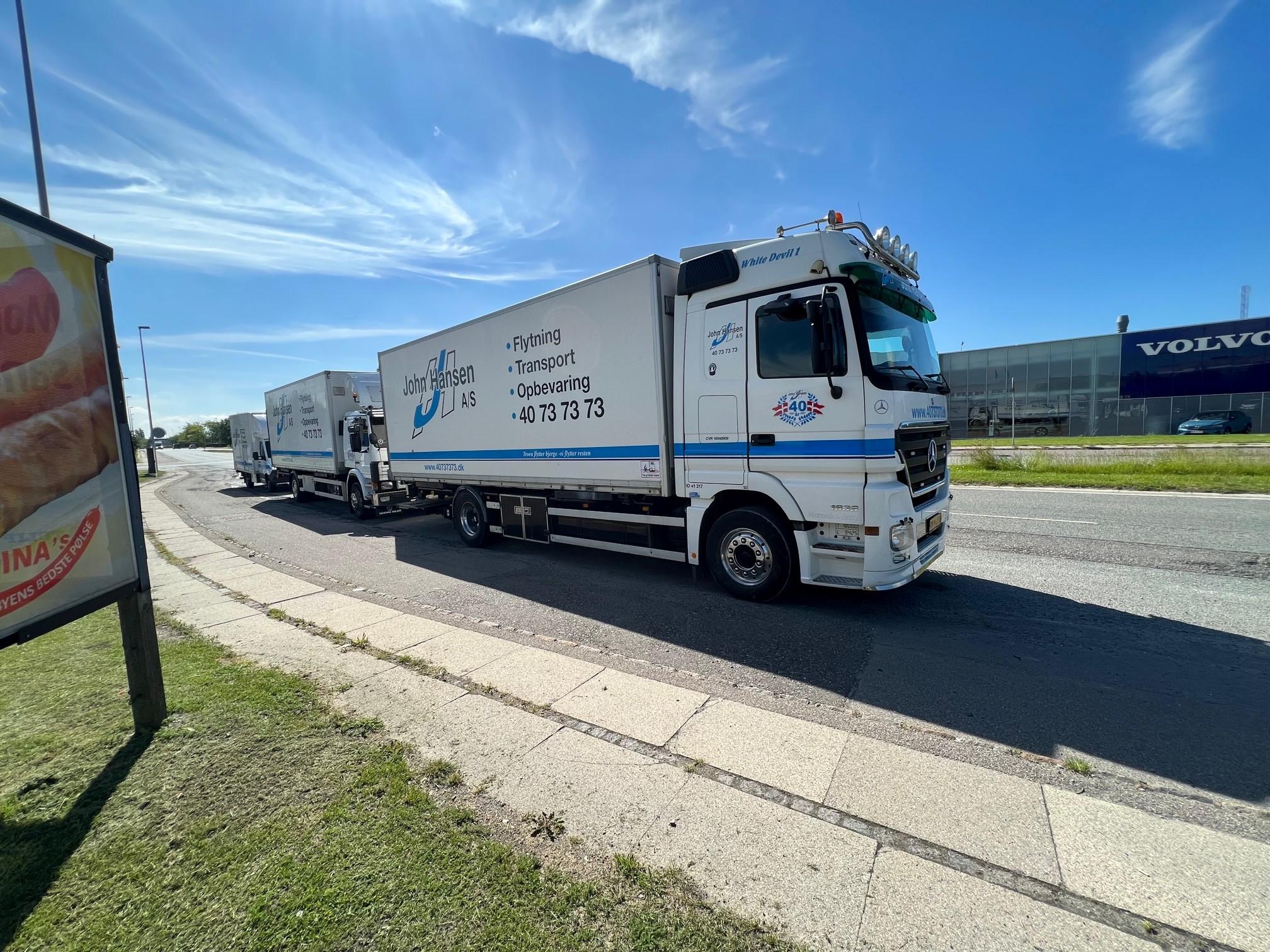 En lastbil parkeret ved vejen med en trailer, der har en hvid farve og logoer på siden.