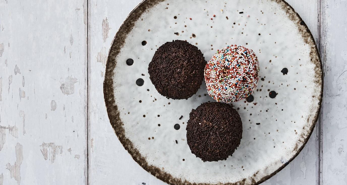Tre chokoladebolde på en hvid tallerken med sorte prikker. En bold er dækket med farverigt drys.