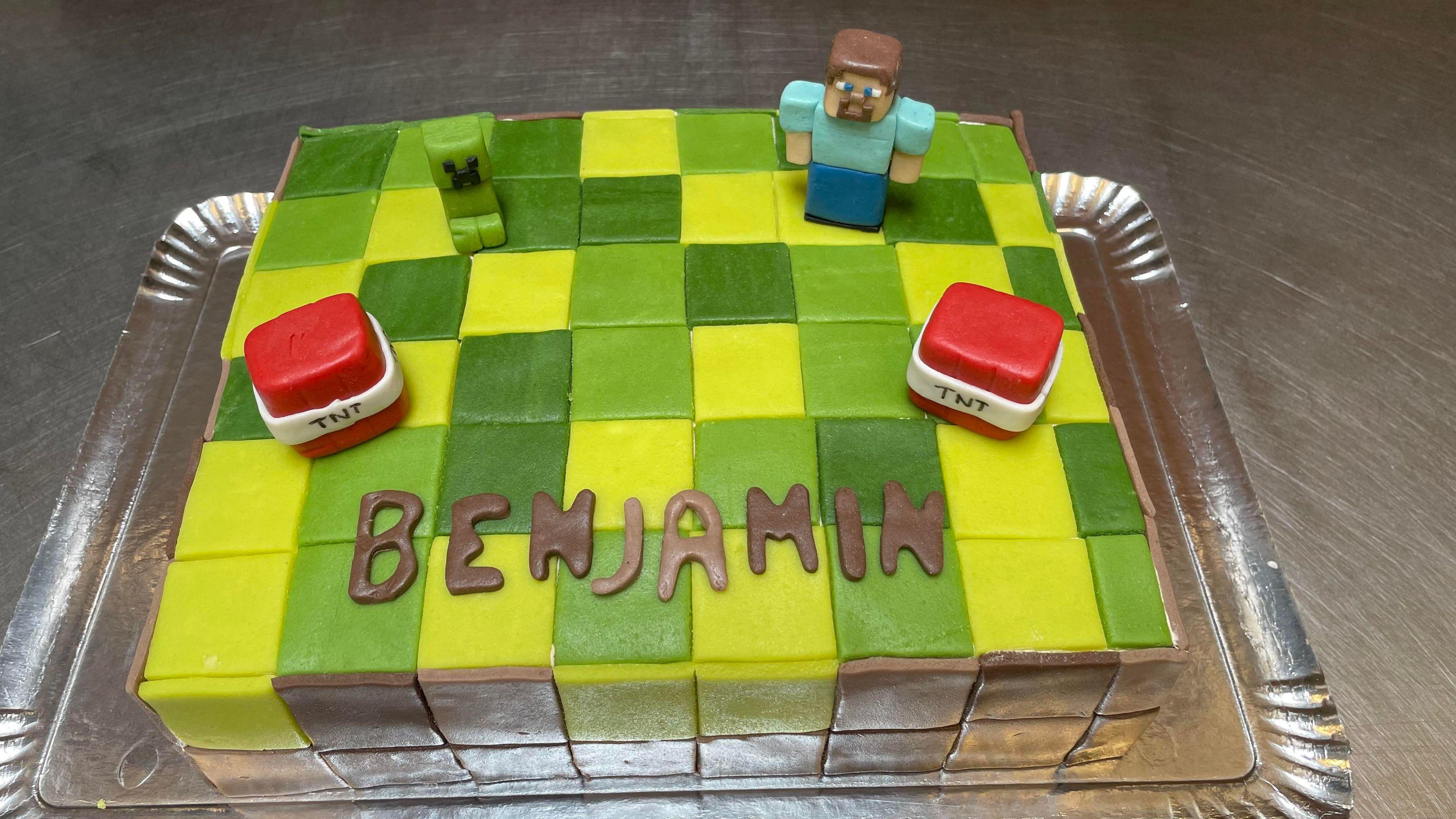 En farverig kage med ternet mønster, en figur fra Minecraft og navnet "BENJAMIN" skrevet på toppen.