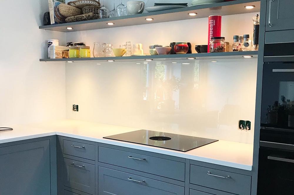Moderne køkken med grå skabe, hvid bordplade og hylde med glas og krydderier.