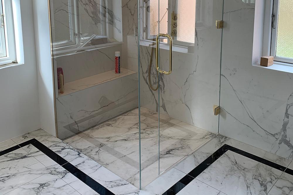 Moderne badeværelse med glasbruser, marmorfliser og elegante detaljer i guld.