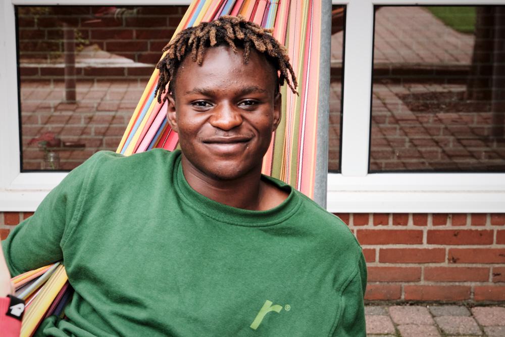Ung mand med dreadlocks sidder afslappet i en hængekøje iført en grøn sweatshirt.
