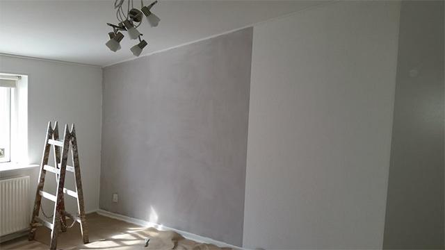 Indendørs rum med grå væg, hvid væg, stige og loftlampe, der belyser området.