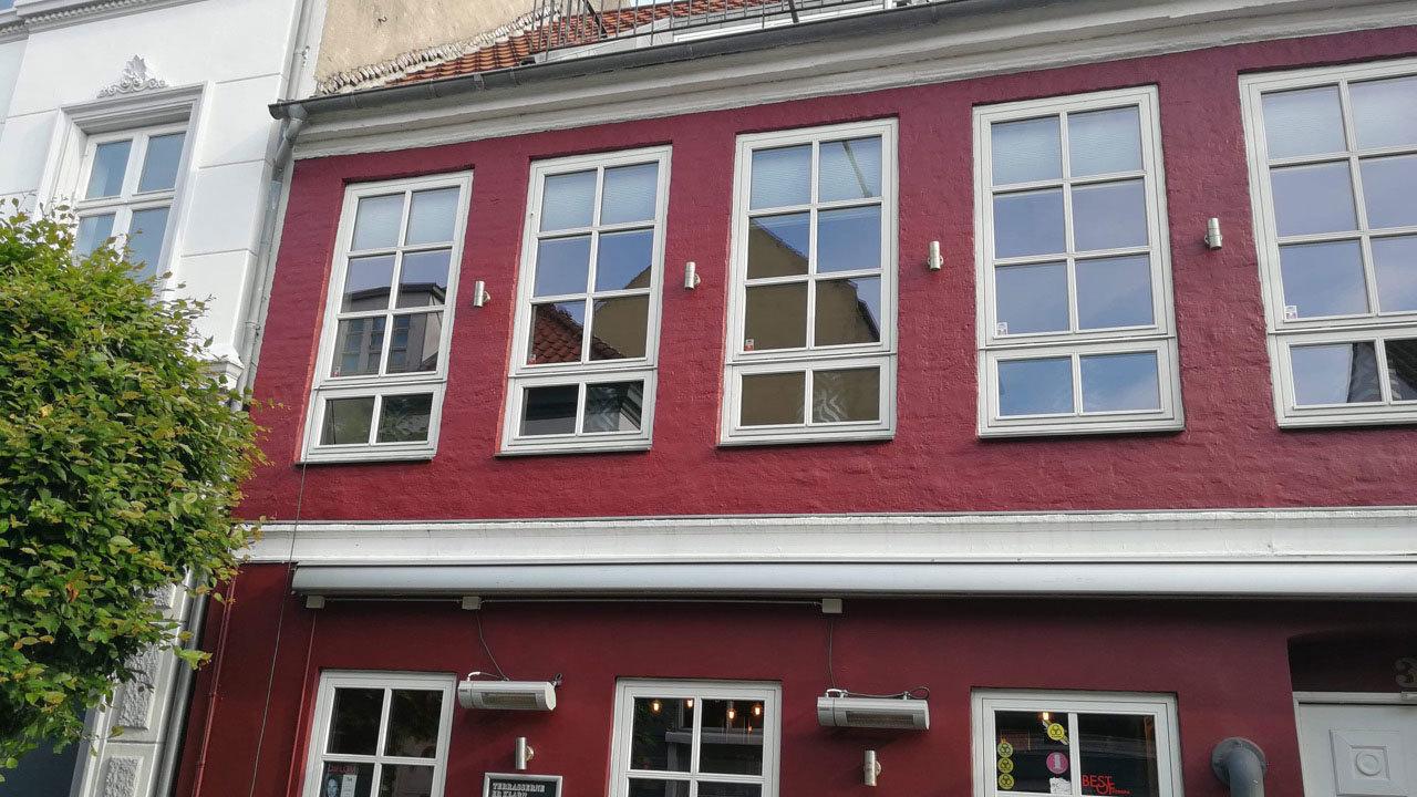 Rød bygning med store vinduer og en hvid facade, beliggende i en bygade.