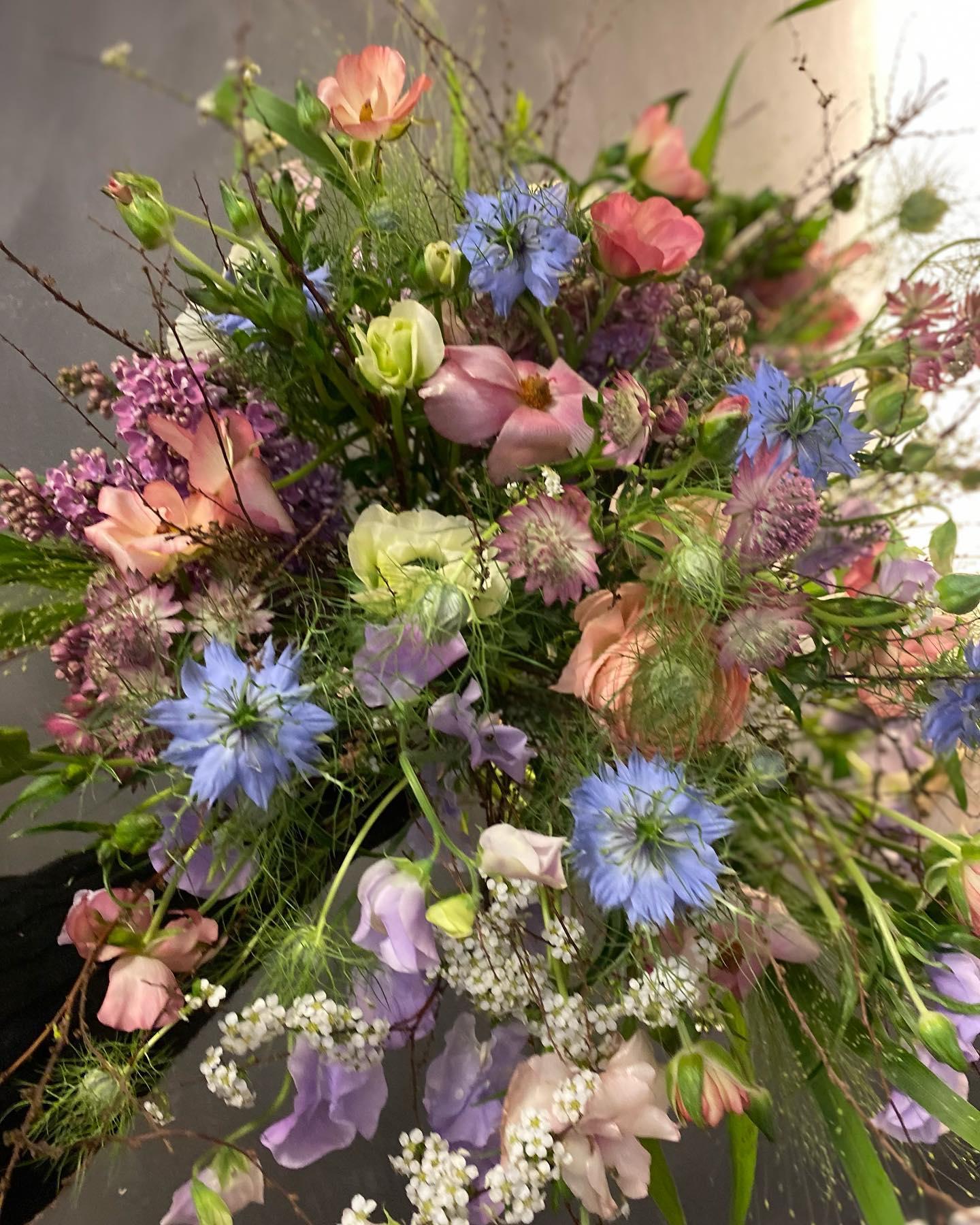 En farverig buket med forskellige blomster som roser, kornblomster og brudeslør i nuancer af pink, blå og lilla.