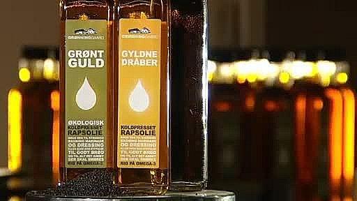 To flasker rapsolie med etiketterne "Grønt Guld" og "Gyldne Dråber" i en butik.