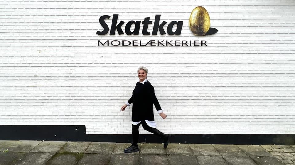 En person går forbi en hvid væg med Skatka Modelækkérers logo.
