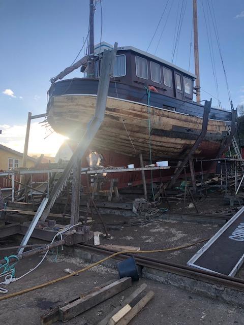 En træbåd på en skibsværft, hævet over jorden med værktøj og materialer omkring.