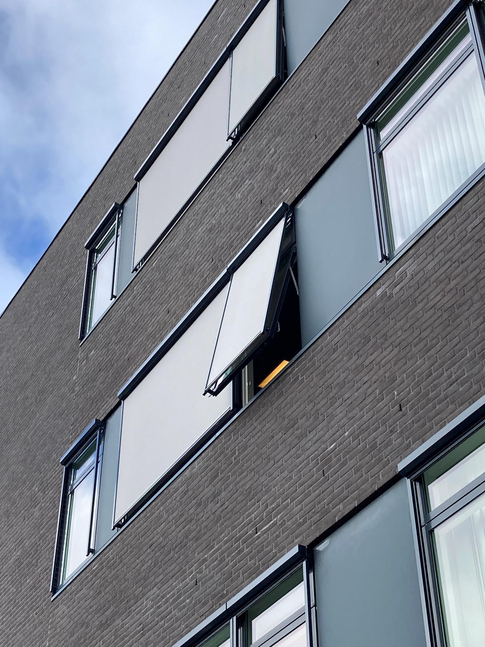 En moderne bygning med grå mursten og vinduer, hvor et vindue er åbent med en markise.