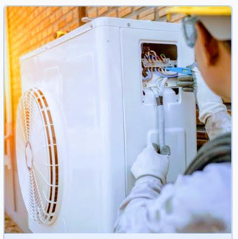 En tekniker arbejder på en udendørs airconditionenhed med værktøj og ledninger.
