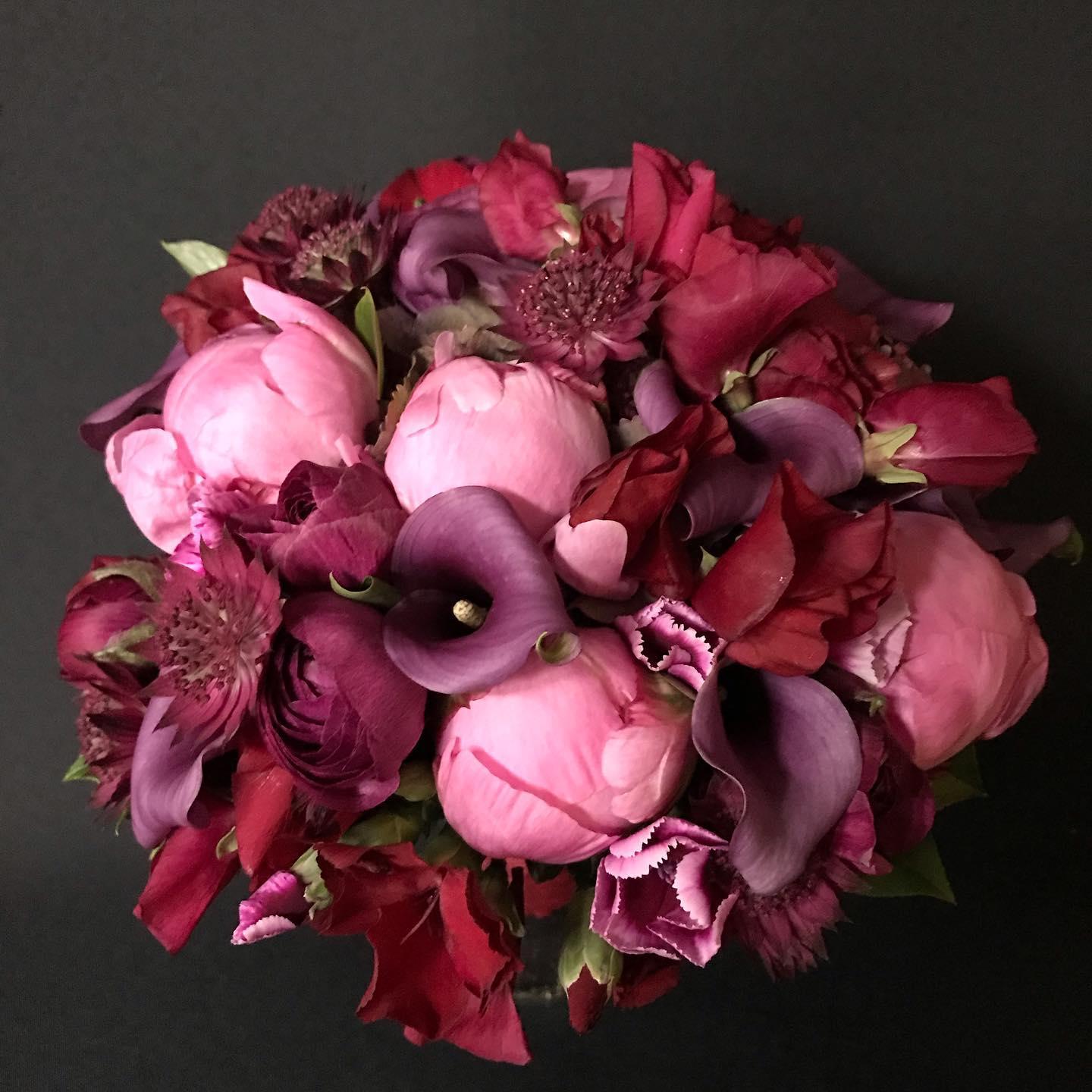 En smuk buket med lyserøde og mørkerøde blomster, herunder pæoner, liljer og forskellige blomster.