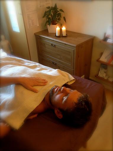 Mand får massage i et afslappende rum med stearinlys og en plante i baggrunden.