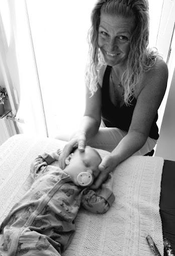 En glad kvinde holder en baby med sut, mens de sidder på en hvid dug ved vinduet.
