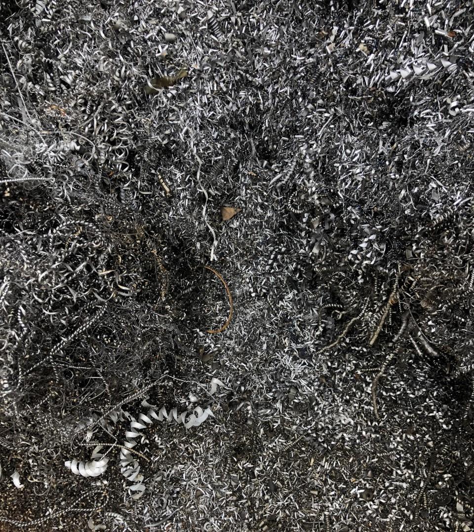 Et tæt lag af grå og sort metalspåner på en overflade med spor af små, hvide skaller.
