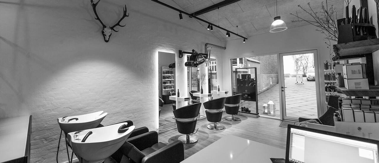 En moderne frisørsalon med sorte stole, vaskestationer og en lys, minimalistisk indretning.