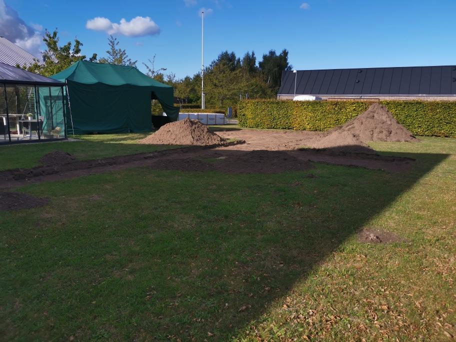 En græsplæne med to jordhøje og en grøn teltstruktur i baggrunden under en blå himmel.