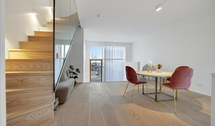 Moderne stue med trappe, spisebord og stole, store vinduer og lys indretning.
