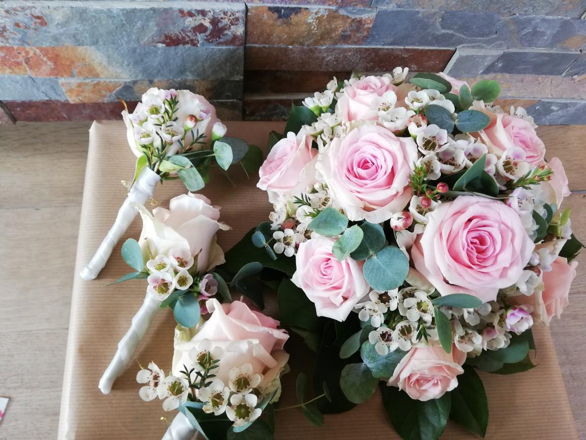 En buket med lyserøde roser og små blomster, samt tre boutonnieres med roser og grønne blade.