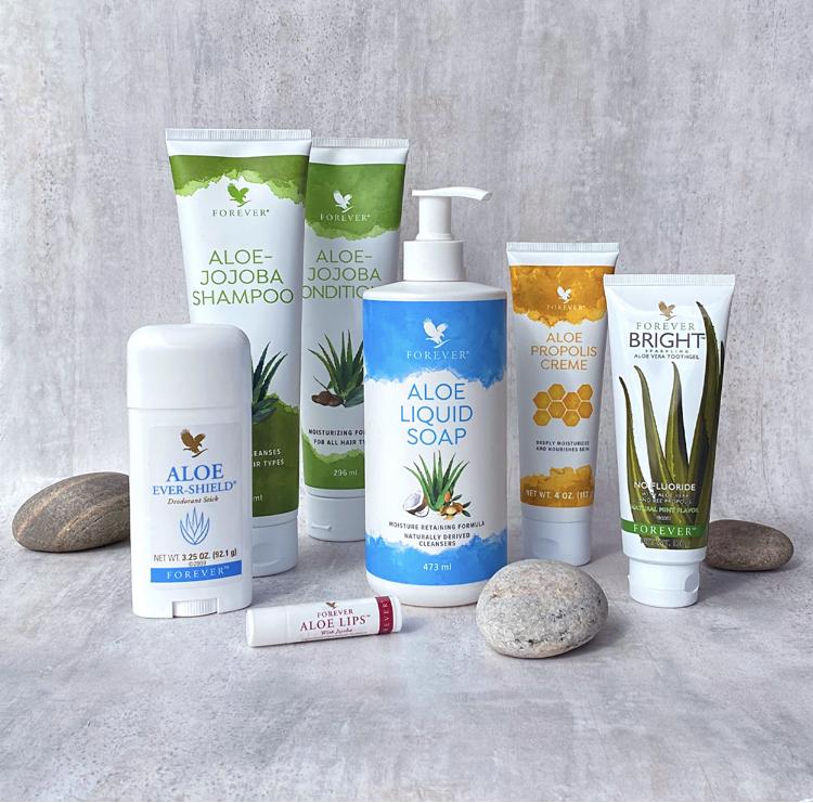 Billede af forskellige aloe vera produkter, herunder shampoo, sæbe og ansigtscreme, præsenteret med sten.